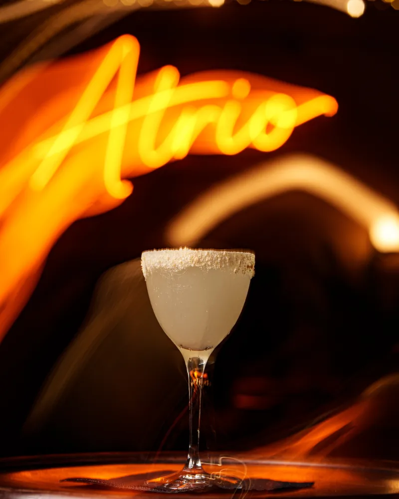 Salt-rimmed cocktail served under the Atrio neon sign