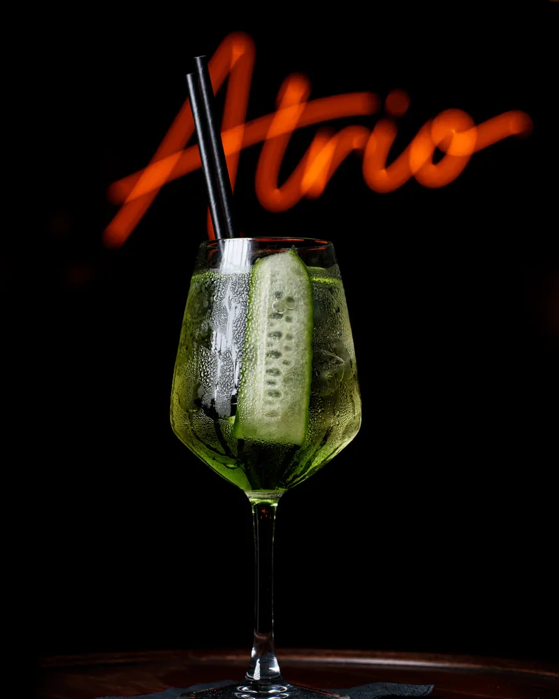 Cucumber and gin cocktail under the Atrio neon sign