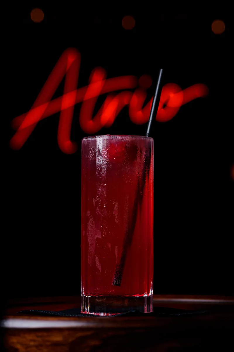 Tall red highball cocktail under the Atrio neon sign